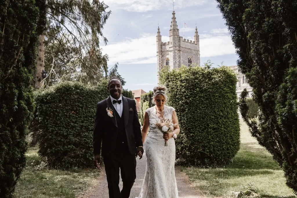 Bride and groom walking hand in hand through church gardens during their Buckinghamshire wedding day.