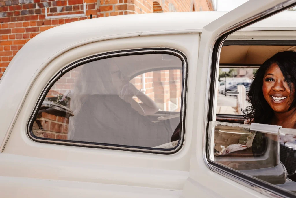 Smiling bridesmaid looking out from a vintage wedding car outside Beaconsfield Registry Office after the ceremony in Buckinghamshire.