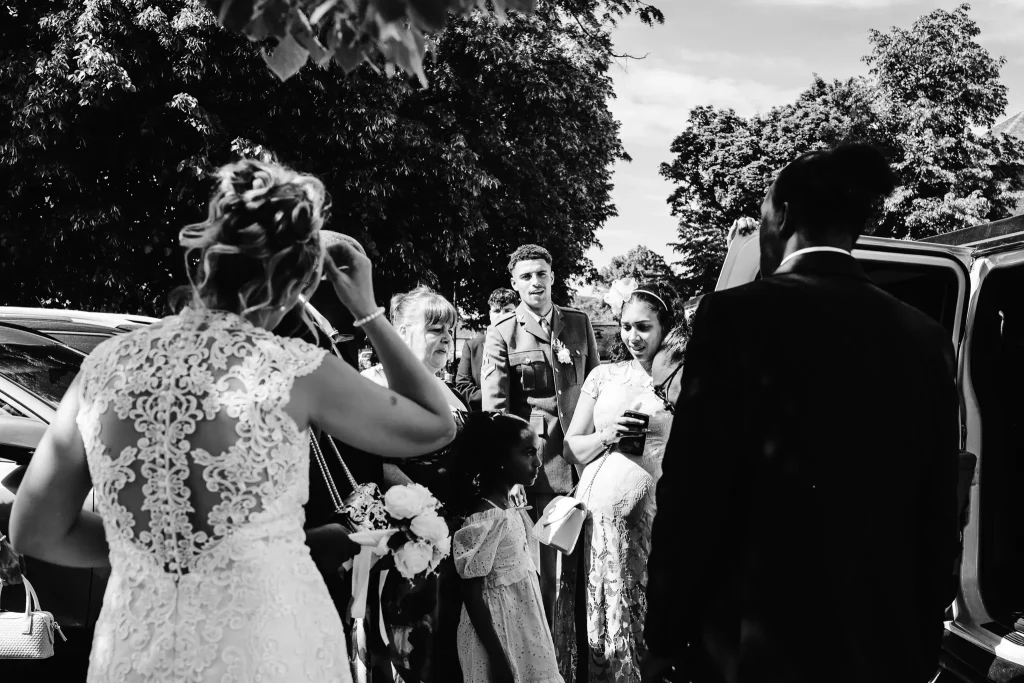 Black and white documentary wedding photograph of guests gathering outside Beaconsfield Registry Office after the ceremony, sharing congratulations and celebrating with the newlyweds.