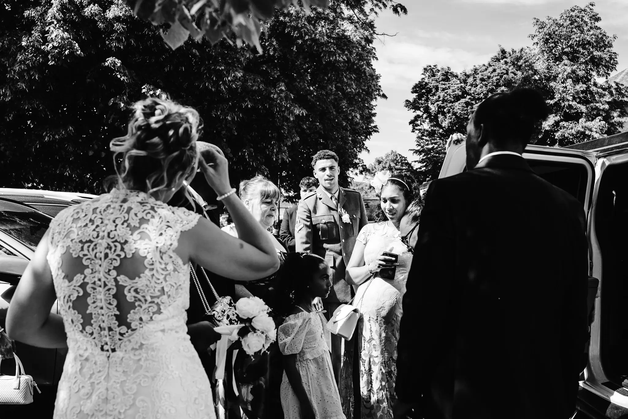 Black and white documentary wedding photograph of guests gathering outside Beaconsfield Registry Office after the ceremony, sharing congratulations and celebrating with the newlyweds.
