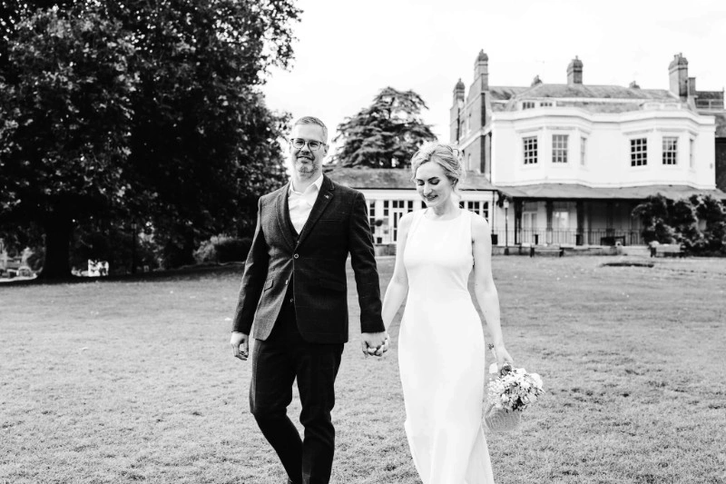 Bride and groom walking hand in hand across the grounds of Higgerson Park in Marlow